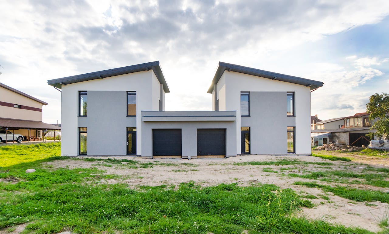 Front view of twin modern houses with a symmetrical architectural design under a cloudy sky.