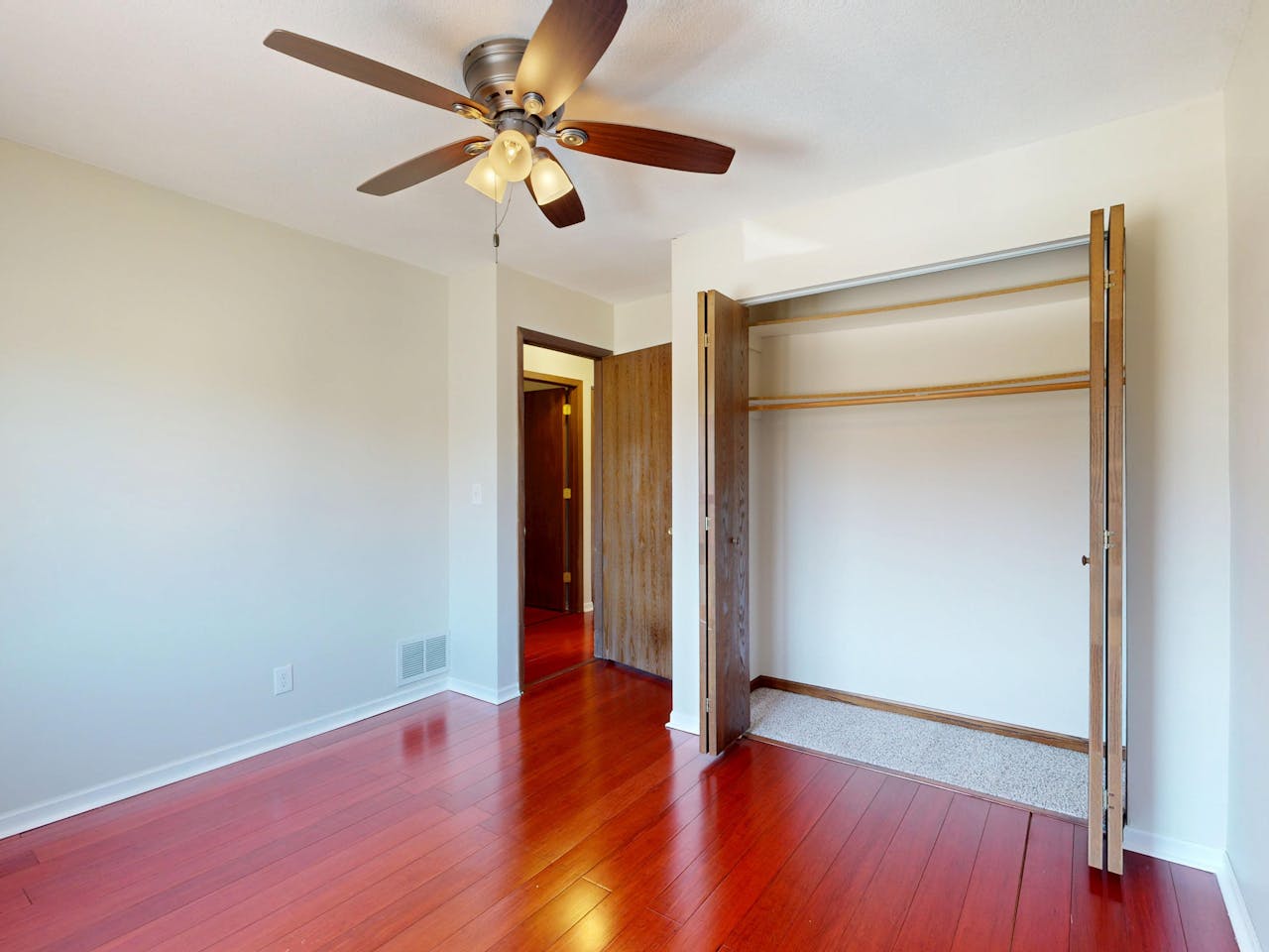 Spacious empty room with hardwood floors, a ceiling fan, and an open closet.