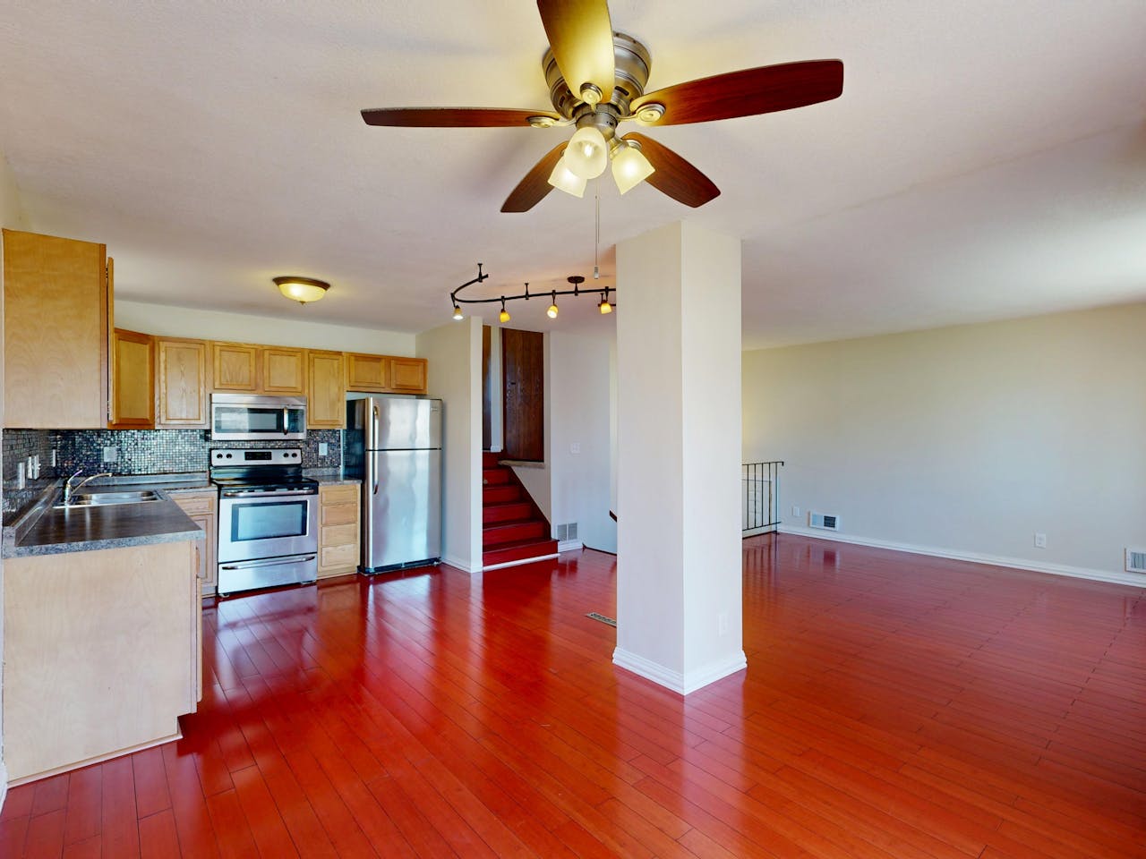 Spacious open-plan kitchen and living room with wood floors and ceiling fan.